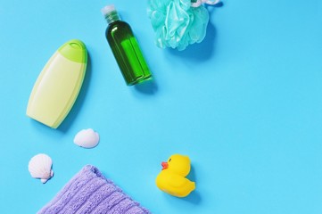 Flat lay bathroom items. Green shampoo bottle or body lotion, sponge, essentials oil, seashells, cotton towel and rubber duck toy on a blue background. Top view photo