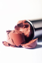 A nude color lipstick being smashed onto a white background showing texture.  Shallow depth of field.  Vertical image.