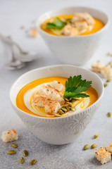 Pumpkin soup with cream, croutons, pumpkin seeds and parsley on a gray concrete or stone background, selective focus