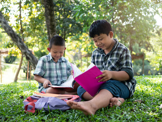 Cute two asian student boy reading book in the nature park with sunlight  background, people, learning, relax, education and Natural classroom concept..