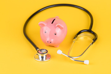 Sparschwein mit Stethoskop vor gelbem Hintergrund