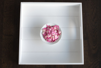 Rosafarbene Rosenblätter in weißer Schale auf weißem Tablett