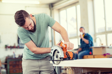 young worker in a carpenter's workshop with hand saw