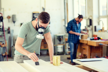 young worker in a carpenter's workshop painting wood with brush and respirator