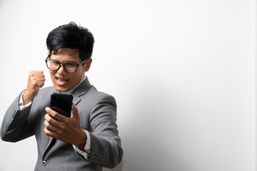 A business man is showing glad and success expression while looking at the smartphone on left hand and make a fist on righthand. More space.