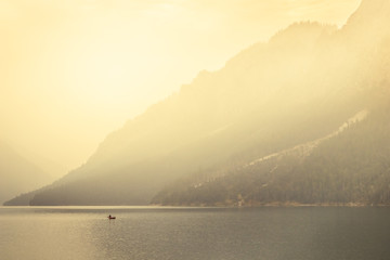 Fototapeta na wymiar Man rowing a small boat on lake Plansee in the European Alps, in Austria at early morning sunrise