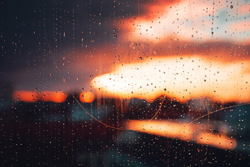 Macro close up of ain water drops on a skratchy window view with colorful sunset city skyline blurry background and moody color tones. Braunschweig, Lower Saxony in Germany