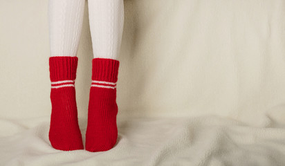 Obraz na płótnie Canvas Female legs in warm white knitted tights and red socks on a white background made of faux fur