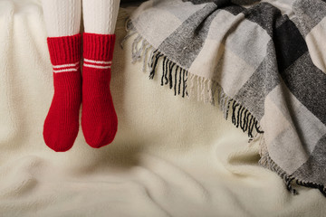 Female legs in warm white knitted tights and red socks on a white background made of faux fur