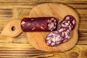 Sliced salami sausage on cutting board on wooden table. Top view