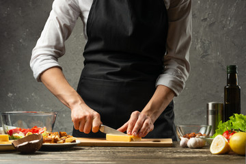Chef cuts mozzarella cheese for pasta. Pizza, salad, Italian culinary recipe concept, on the background of a concrete wall