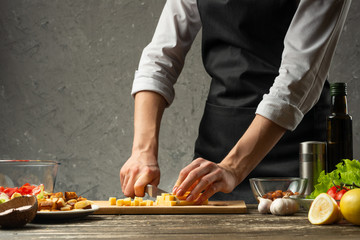 Chef cuts mozzarella cheese for pasta. Pizza, salad, Italian culinary recipe concept, on the background of a concrete wall