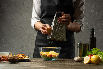 Chef throwing cheese into a bowl of Greek salad and seafood, cooking, restaurant concept, against a concrete wall with space for text