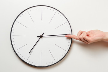 Woman hand stop time on round clock, female finger takes the minute arrow of the clock back, time...