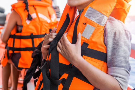 Asian female in life jacket with other people near sea on ship