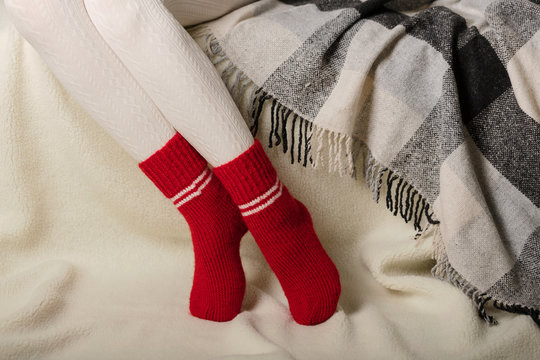 Female legs in warm white knitted tights and red socks on a white background made of faux fur.