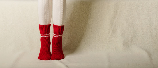 Female legs in warm white knitted tights and red socks on a white background made of faux fur