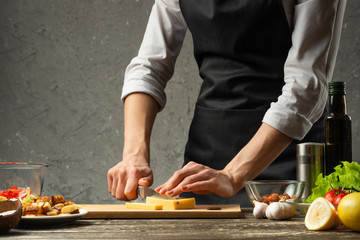 Chef cuts mozzarella cheese for pasta. Pizza, salad, Italian culinary recipe concept, on the background of a concrete wall