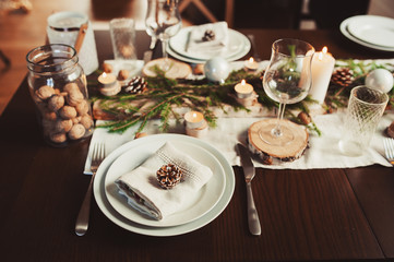Festive Christmas and New Year table setting in scandinavian style with rustic handmade details in natural and white tones. Dining place decorated with pine cones, branches and candles