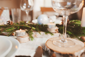 Festive Christmas and New Year table setting in scandinavian style with rustic handmade details in natural and white tones. Dining place decorated with pine cones, branches and candles