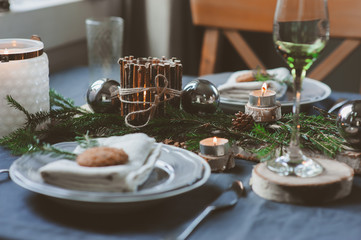 Festive Christmas and New Year table setting in scandinavian style with rustic handmade details in natural and white tones. Dining place decorated with pine cones, branches and candles