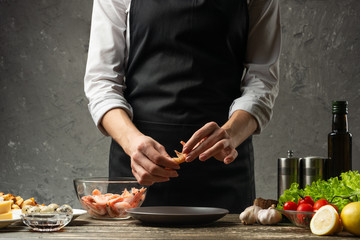 The chef processes shrimps for seafood salad at the home kitchen. Background from a concrete wall with a text area for restaurant menu design