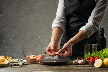 The chef processes shrimps for seafood salad at the home kitchen. Background from a concrete wall with a text area for restaurant menu design