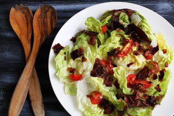 Red lettuce salat in white plate on dark board with cherry tomatoes, bacon and cheese