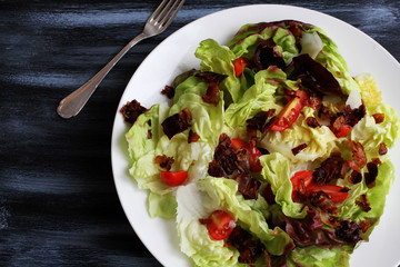 Red lettuce salat in white plate on dark board with cherry tomatoes, bacon and cheese