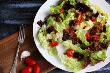 Red lettuce salat in white plate on dark board with cherry tomatoes, bacon and cheese