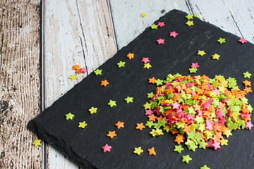 Decorative colorful sugar stars on wooden board with slate, high angle view, close-up
