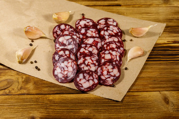 Sliced salami sausage on brown paper on wooden table