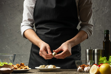 Chef cleans quail eggs for a vegetarian salad with seafood on the background of a concrete wall