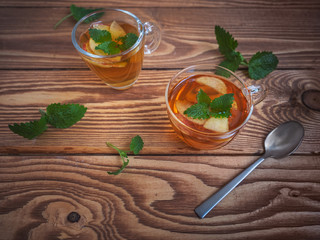 Tea with apples in glass mugs, a teaspoon on a warm wooden background