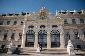 Obraz premium Groom and bride stand on stairs by the great palace in Wiena