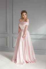 Fototapeta premium Beautiful blonde woman in beige powdery silk wedding dress posing in studio room