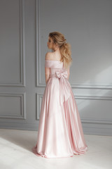 Fototapeta premium Beautiful blonde woman in beige powdery silk wedding dress posing in studio room