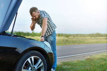 man with a phone in front of the open hood of a broken car
