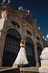 Fototapeta premium Beautiful bride in luxury wedding dress in front of palace