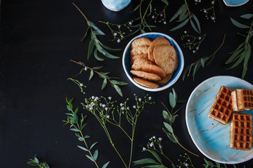 three delicious waffles, gingerbread cookies are the blue plates with herbs and flowers on a black background closeup food photos copyspace