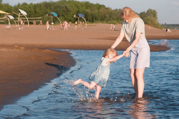 Mom and girl playing on the beach of the river at sunset and swim.