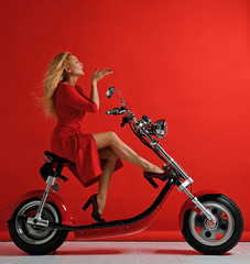 Fototapeta na wymiar Woman ride new electric car motorcycle bicycle scooter present for new year 2019 in red dress blow kiss sign with lips on red