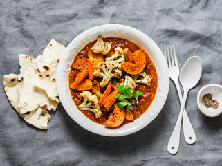 Roasted curry vegetables. Sweet potatoes, cauliflower, carrots, onions, pumpkin with curry sauce on grey background, top view. Vegetarian food concept
