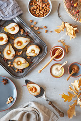 Flat lay with a tray of baked pears with caramelized nuts on gray concrete background