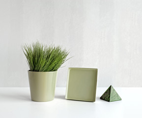 Still life of grass in flowerpot, metal tray and marble pyramid.