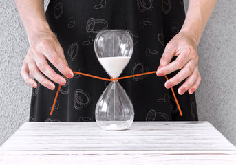Hands tying a red cord on a sand clock stopping time.