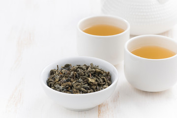 cups and teapot with green tea on a white wooden background, close-up