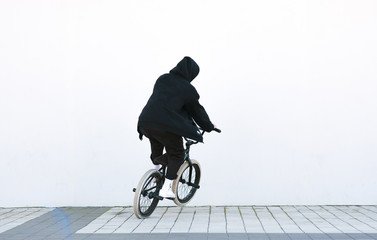 Back of a young man in black clothes, riding a bmx bike on the background of a white wall. Bmx...