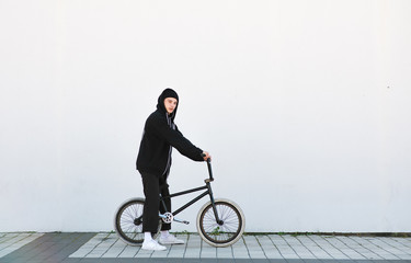 Portrait of a stylish young man with a bmx bike on the background of a white wall. Young rider with bmx bike stands on a white background. BMX concept.