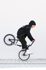 Bmx racer makes a trick in against the background of a white wall. Bmx rider with a bicycle in...